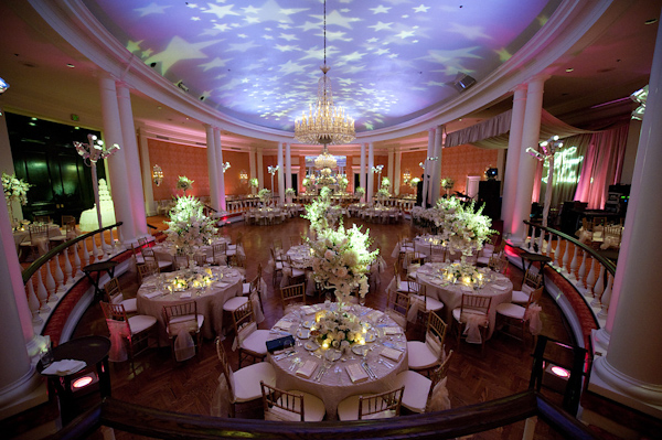 beautiful reception seating area and decor - white floral centerpieces,chandeliers, pink and purple lighting with stars on the ceiling -  photo by Houston based wedding photographer Adam Nyholt 