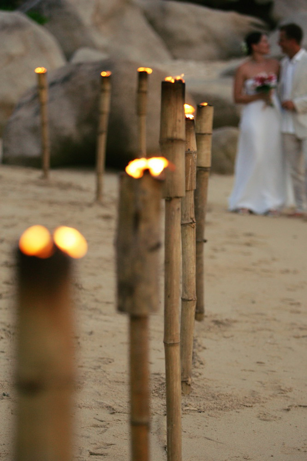 Bride and groom on the beach with rustic bamboo torches - wedding photo by David Beckstead