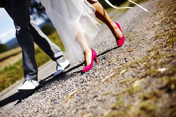 the happy couple walking down road -  red shoes of bride - wedding photo by top Swedish wedding photographers Dayfotografi