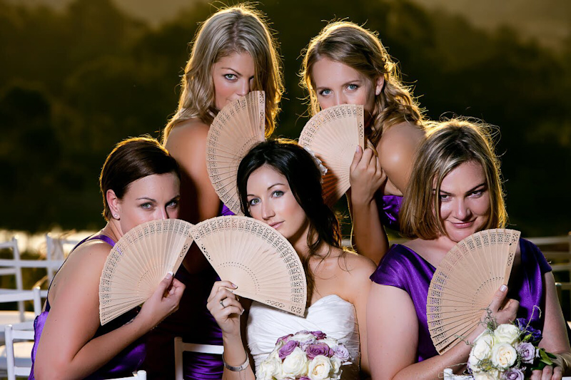 Bride in white dress and bridesmaids in purple dresses holding fans - photo by South Africa based wedding photographer Greg Lumley