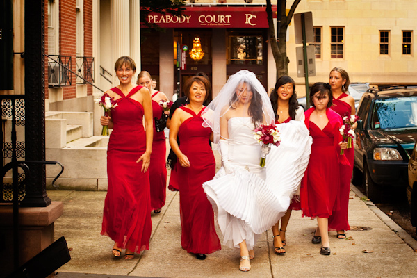 fun photo of the bride in white and her bridesmaids in bright red dresses strutting down an urban sidewalk - photo by Washington DC based wedding photographers Holland Photo Arts