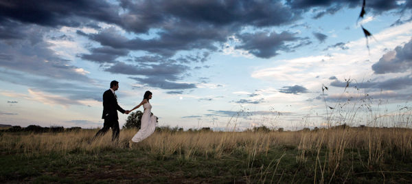gorgeous image of the happy couple walking through an open field holding hands with dramatic clouds above - photo by Italian wedding photographer JoAnne Dunn