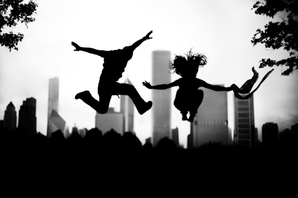 fun engagement shoot - silhouette of couple jumping in front of Chicago skyline - photo by Chicago based wedding photographer Kevin Weinstein 