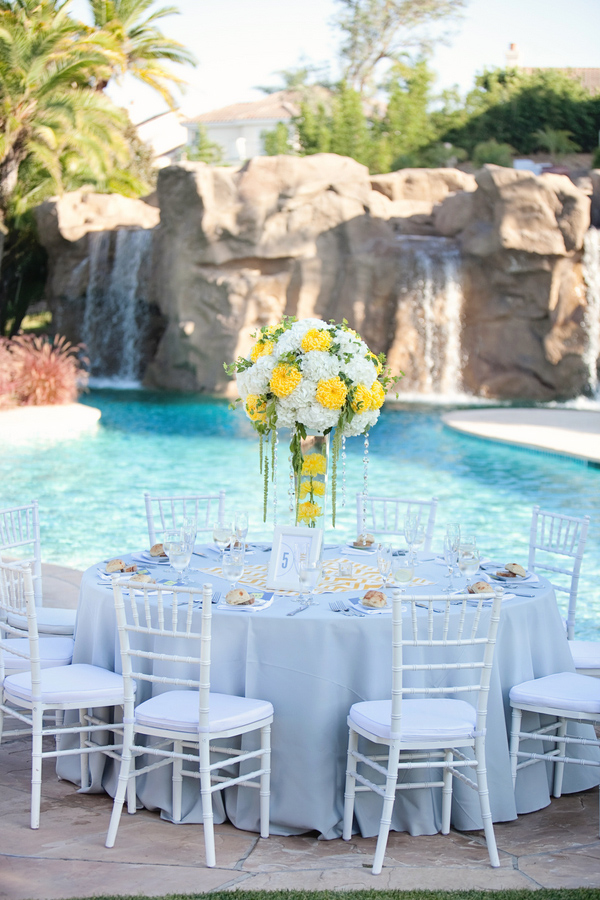 Tall yellow and white centerpiece at a beautiful poolside wedding reception - Photo by April Smith & Co.