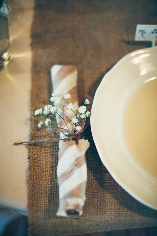 Place setting featuring brown and white striped napkin tied with white flower - Photo by The Schultzes