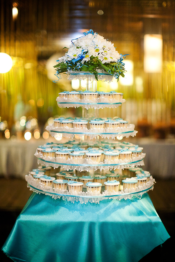 a tiered platform holds blue and white cupcakes with floral detail on top - traditional Indonesian wedding in Bali - photo by Portland wedding photographer Bunn Salarzon