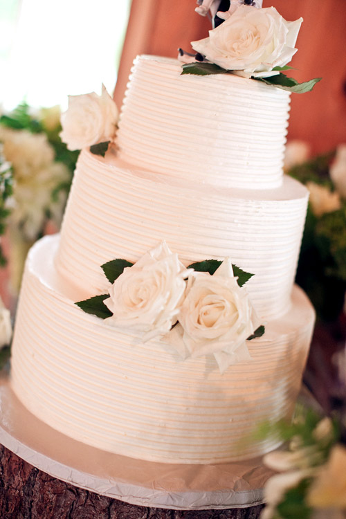 Three-tiered white wedding cake with decorative roses - Photo by Emily Delamater