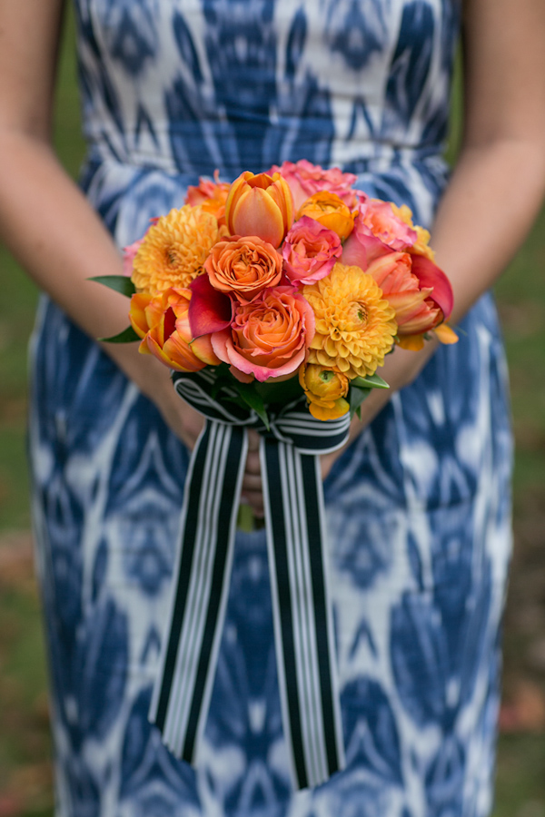 Vibrant orange bridesmaid bouquet paired with blue and white dress and black and white ribbon - Photo by Sarah Tew Photography