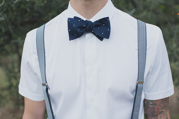 Groom wearing white button up short sleeve short with blue and white polka dot bowtie and blue suspenders - Photo by Whitewall Photography
