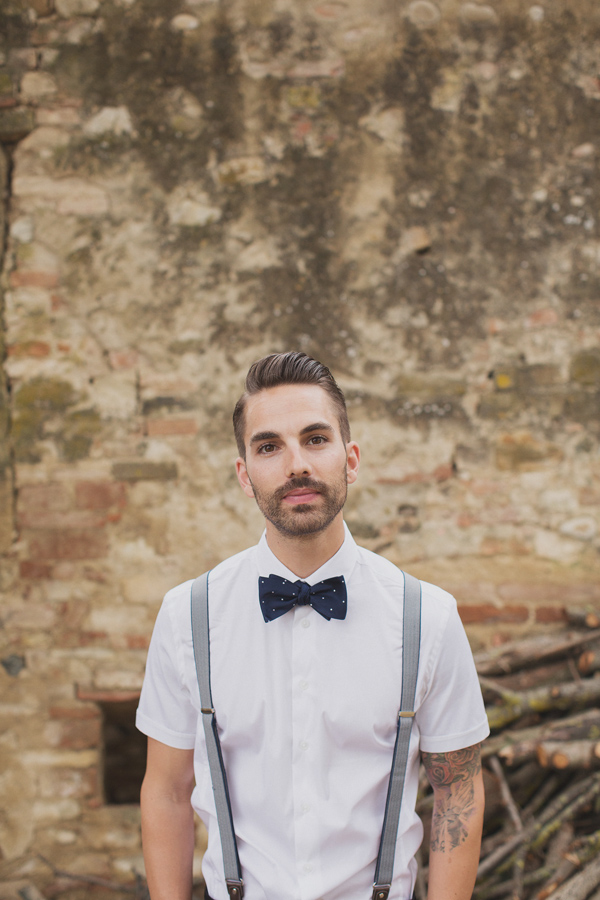 Dapper groom wearing short sleeve white button up shirt, navy bowtie and blue suspenders - Photo by Whitewall Photography