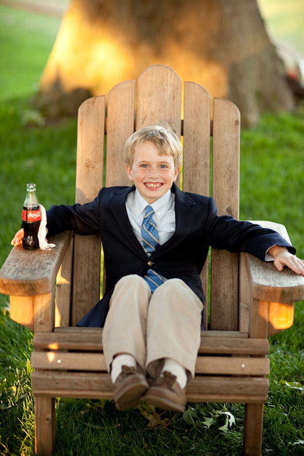 adorable ring bearer wearing a tan slacks, a dark blue sports coat, and light blue tie sitting in a lawn chair - photo by Washington DC wedding photojournalist Paul Morse