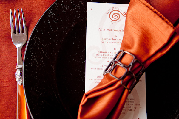 table setting details - black plate on a red-orange tablecloth with ivory and orange dinner menu and orange napkin - photo by New Mexico based wedding photographers Twin Lens