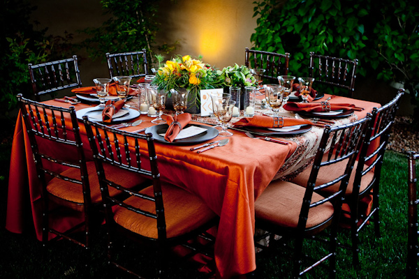 outdoor reception table setting - orange tablecloth and napkins, black chairs and plates, and a yellow, orange, and green centerpiece - photo by New Mexico based wedding photographers Twin Lens