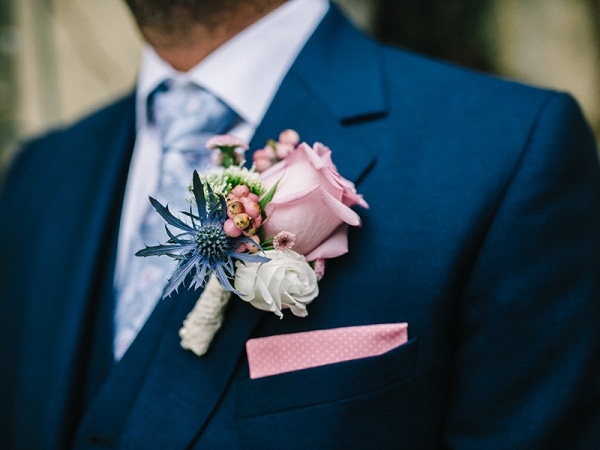 pink rose boutonniere with blue and ivory flowers on a navy suit