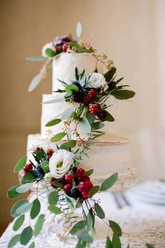 partially iced three tier wedding cake with eucalyptus and berries