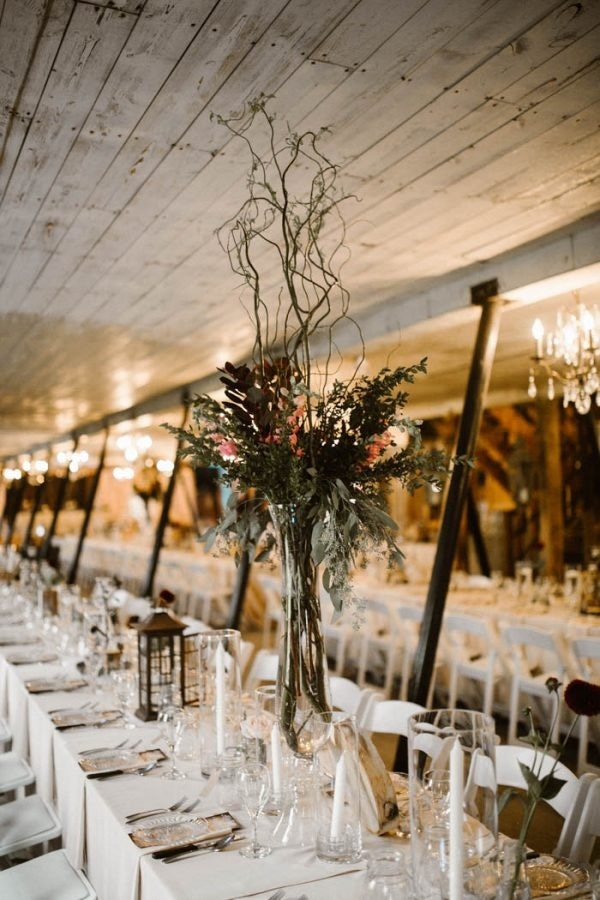 Barn Reception Table Setting with Lanterns, Clear Glass Vases, and Tall Floral Arrangements