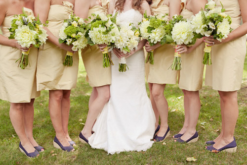 Bridesmaids wearing ivory dresses and navy wedges holding green and ivory bouquets - Photo by Emily Delamater