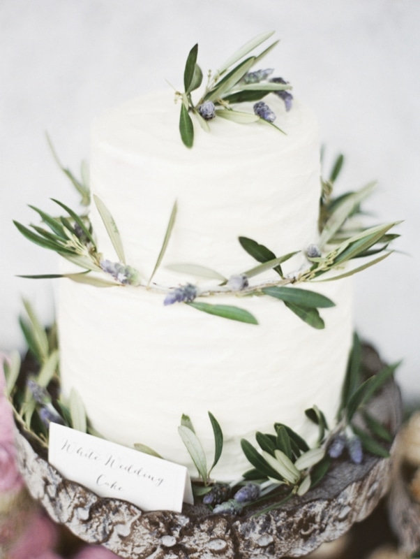 white cake on wood platterwith accents of herbs and berries, photo by Erich McVey Photography