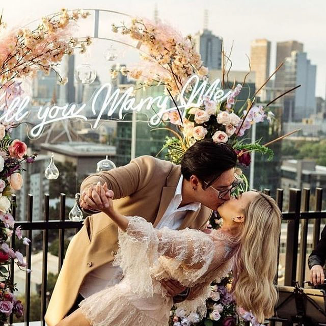 couple kissing in front of proposal sign