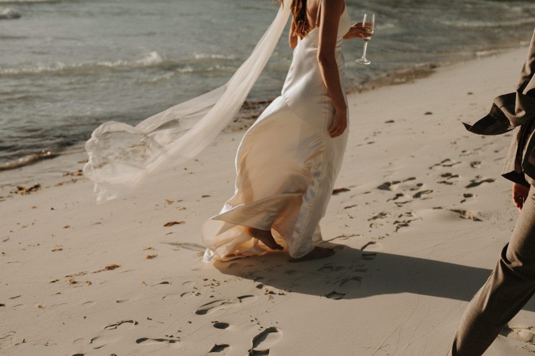 bride walking on beach with wine glass