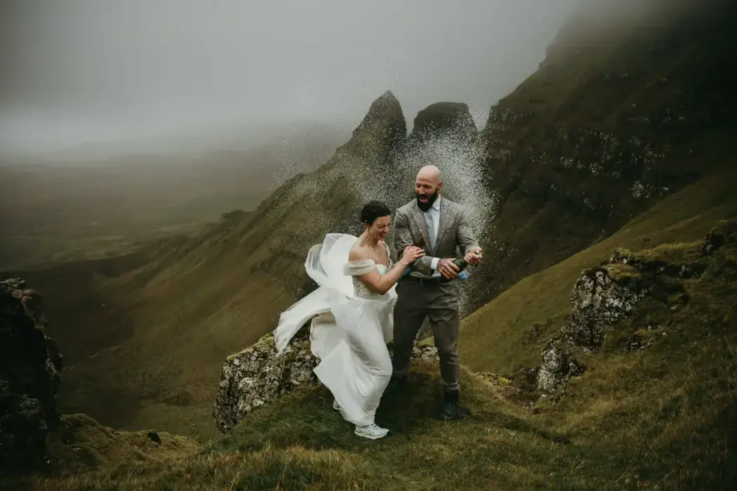 Wedding couple on Scotland mountain popping champagne