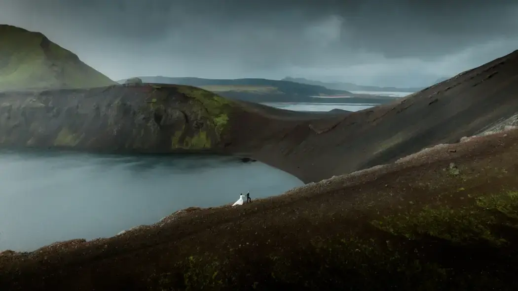 moody wide shot Iceland and tiny wedding couple climbing mountain