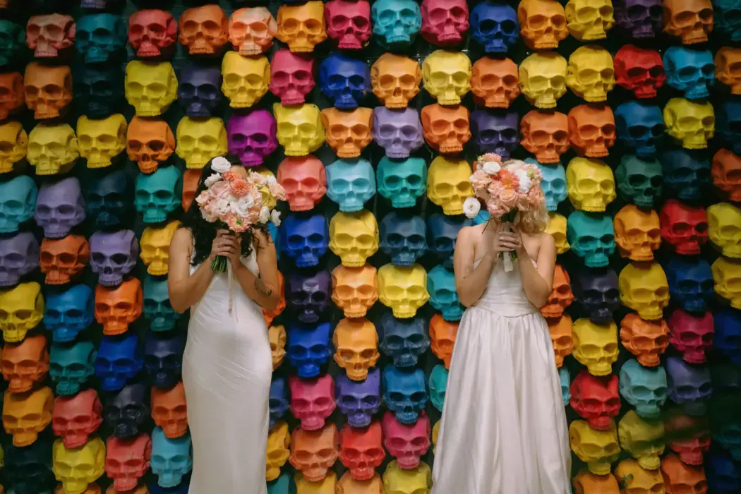 two brides standing in front of a wall with colorful skulls