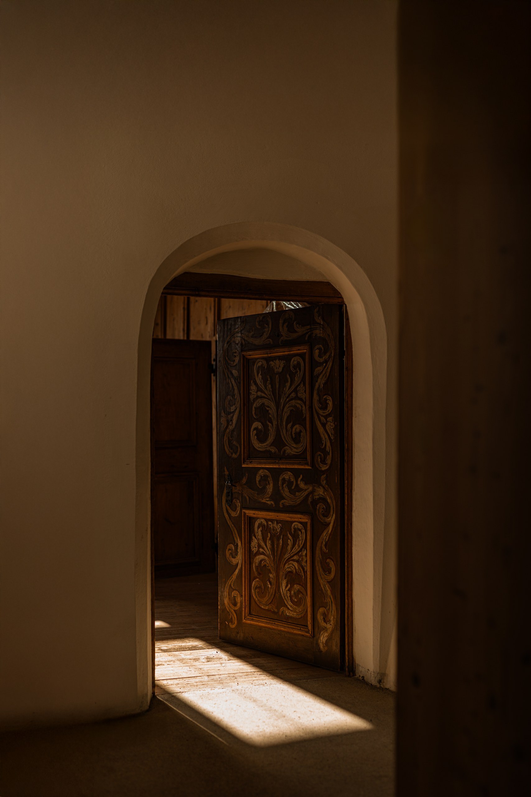 Sunlight falling through an arched doorway onto an ornately carved antique wooden door at Castel Badia