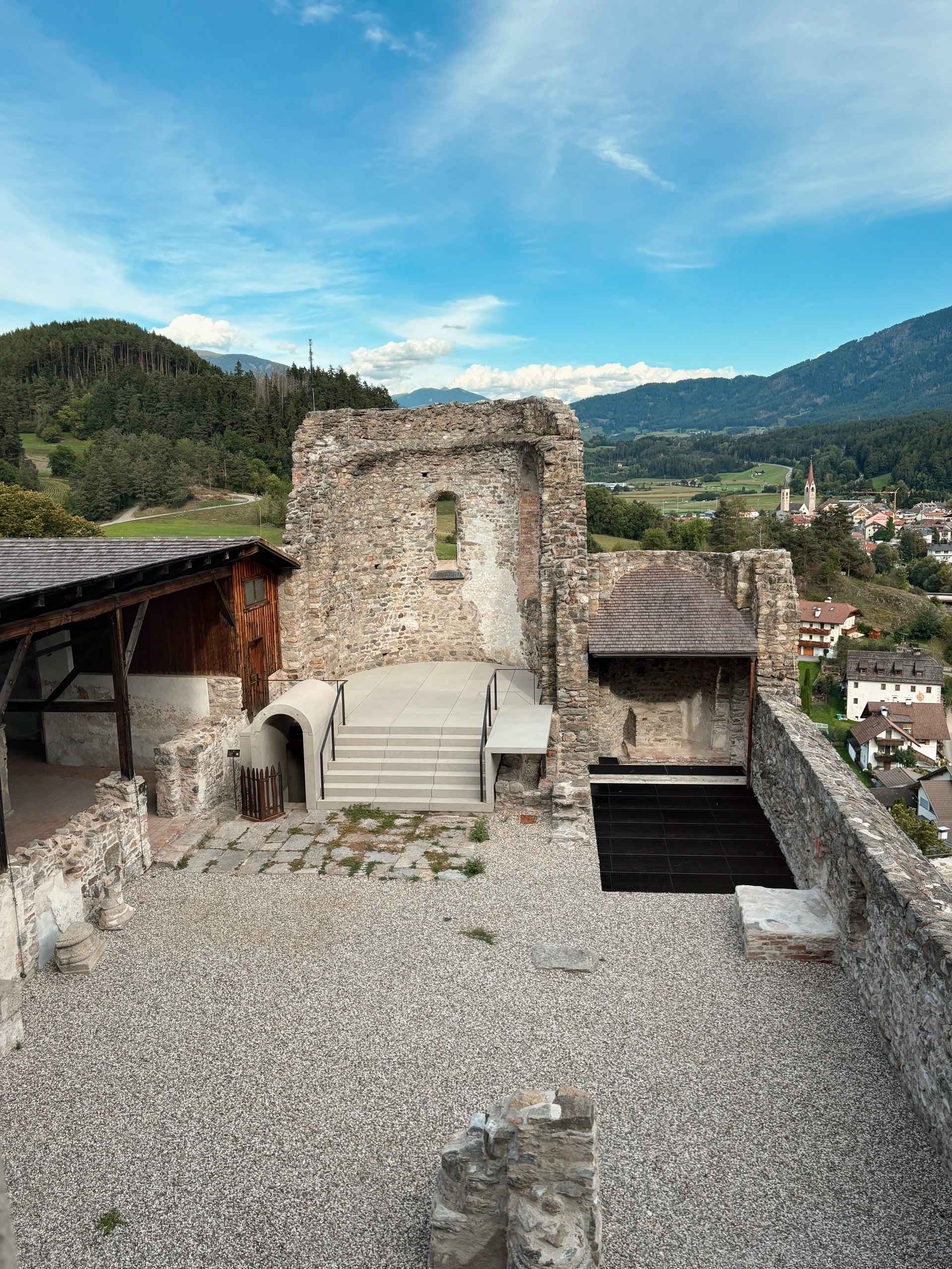 View over the chapel ruins and gravel courtyard at Castel Badia toward a village and the valley beyond