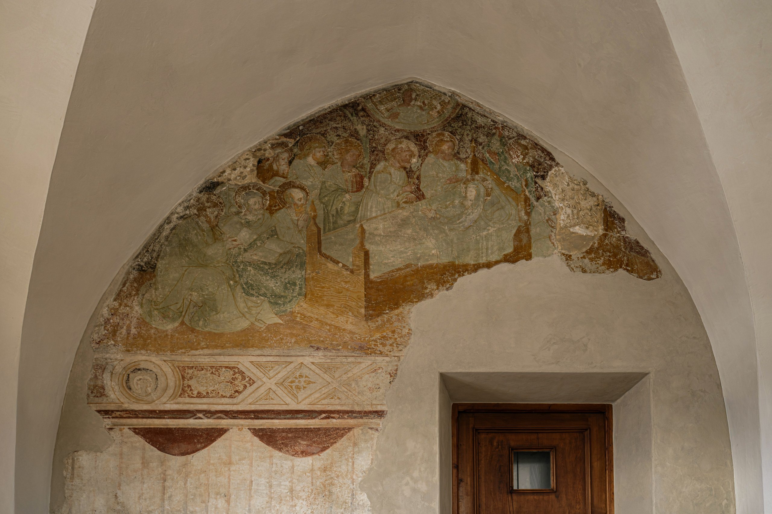 Faded medieval fresco in a vaulted arch above a wooden door at Castel Badia