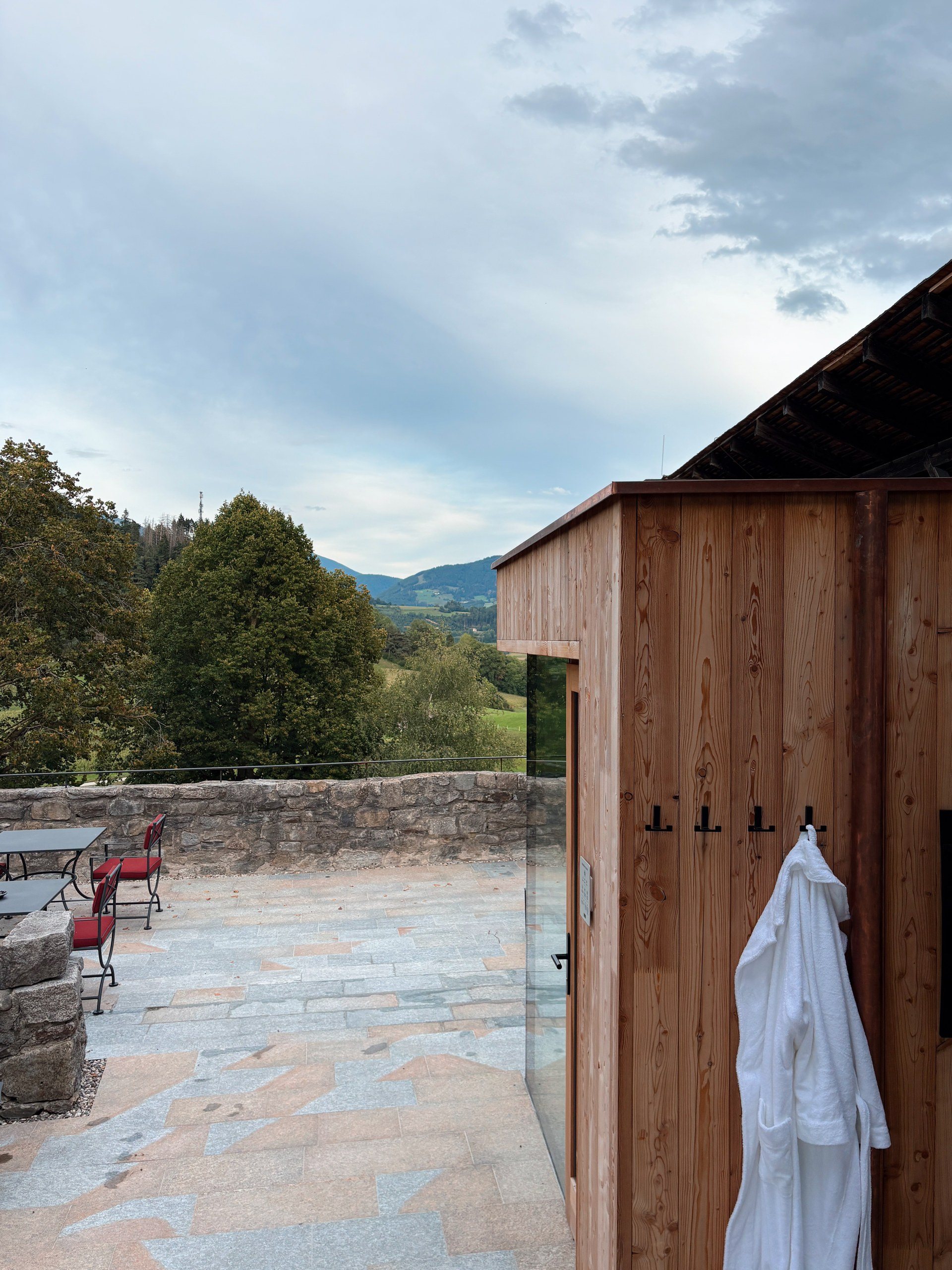 Outdoor wooden sauna with a white robe hanging outside on a stone terrace at Castel Badia