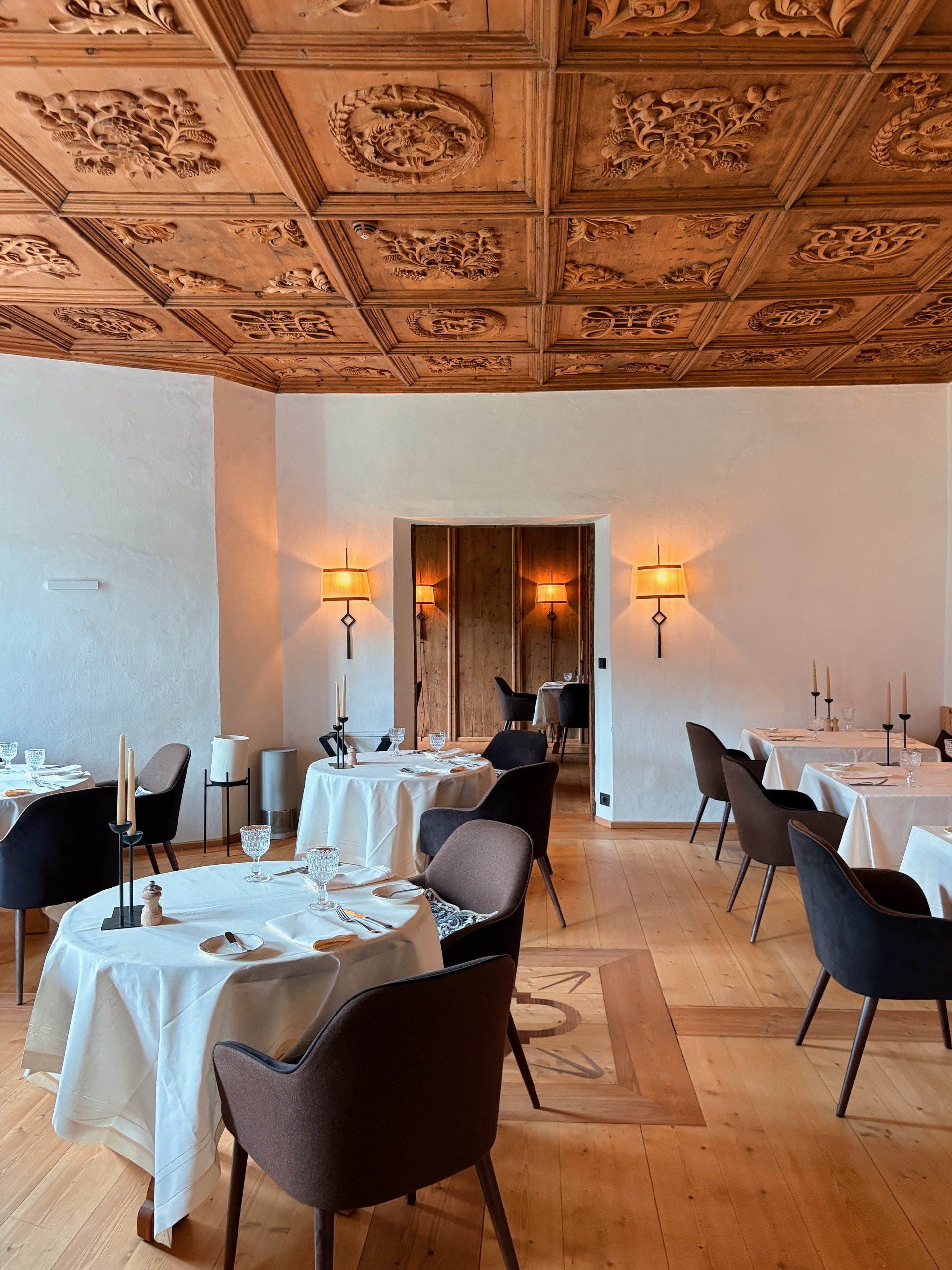 Castel Badia restaurant in daylight with white-clothed tables under an ornately carved wooden ceiling