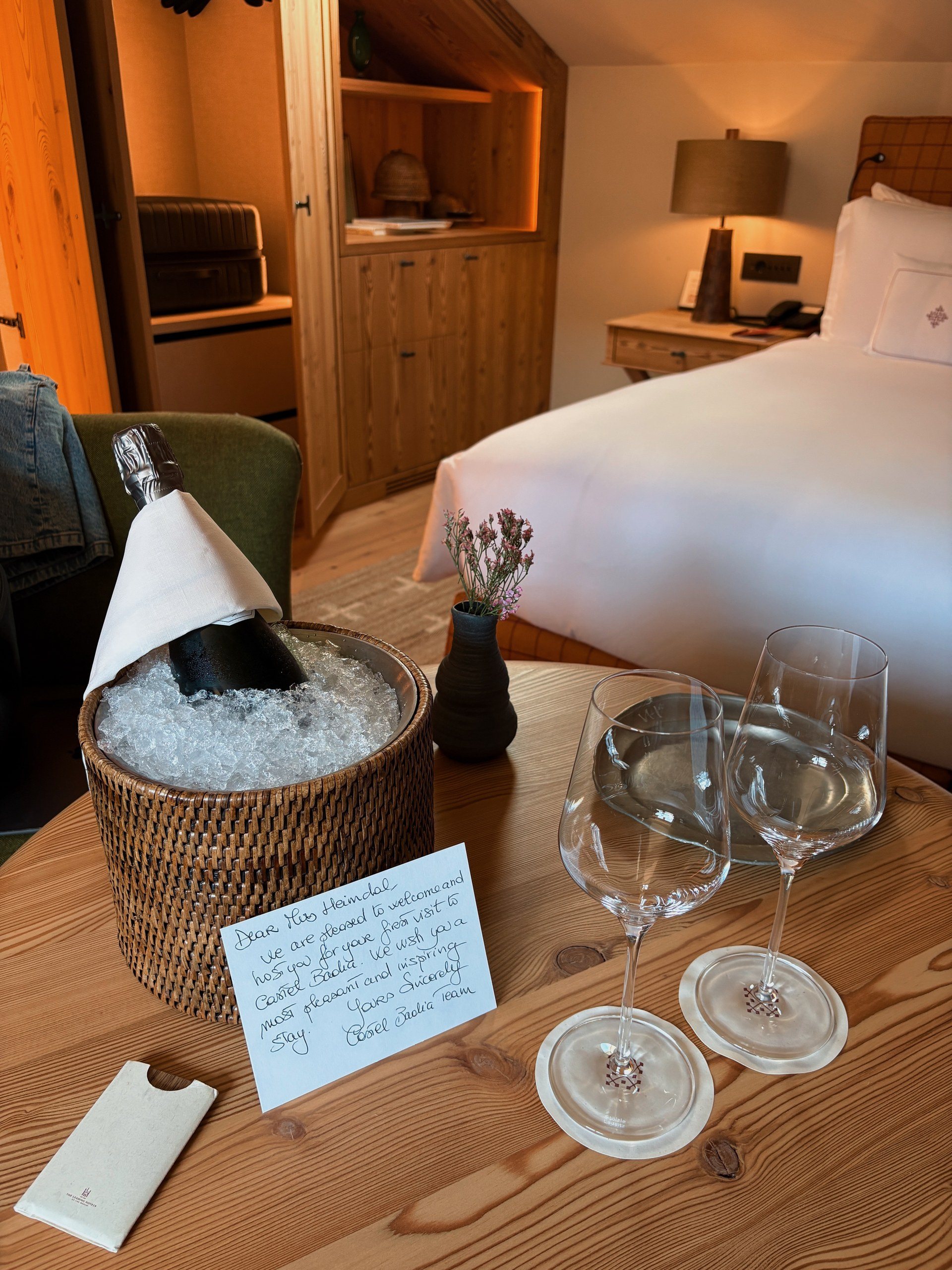 Welcome amenity in a Castel Badia suite with sparkling wine on ice, two glasses, and a handwritten note on a wooden table