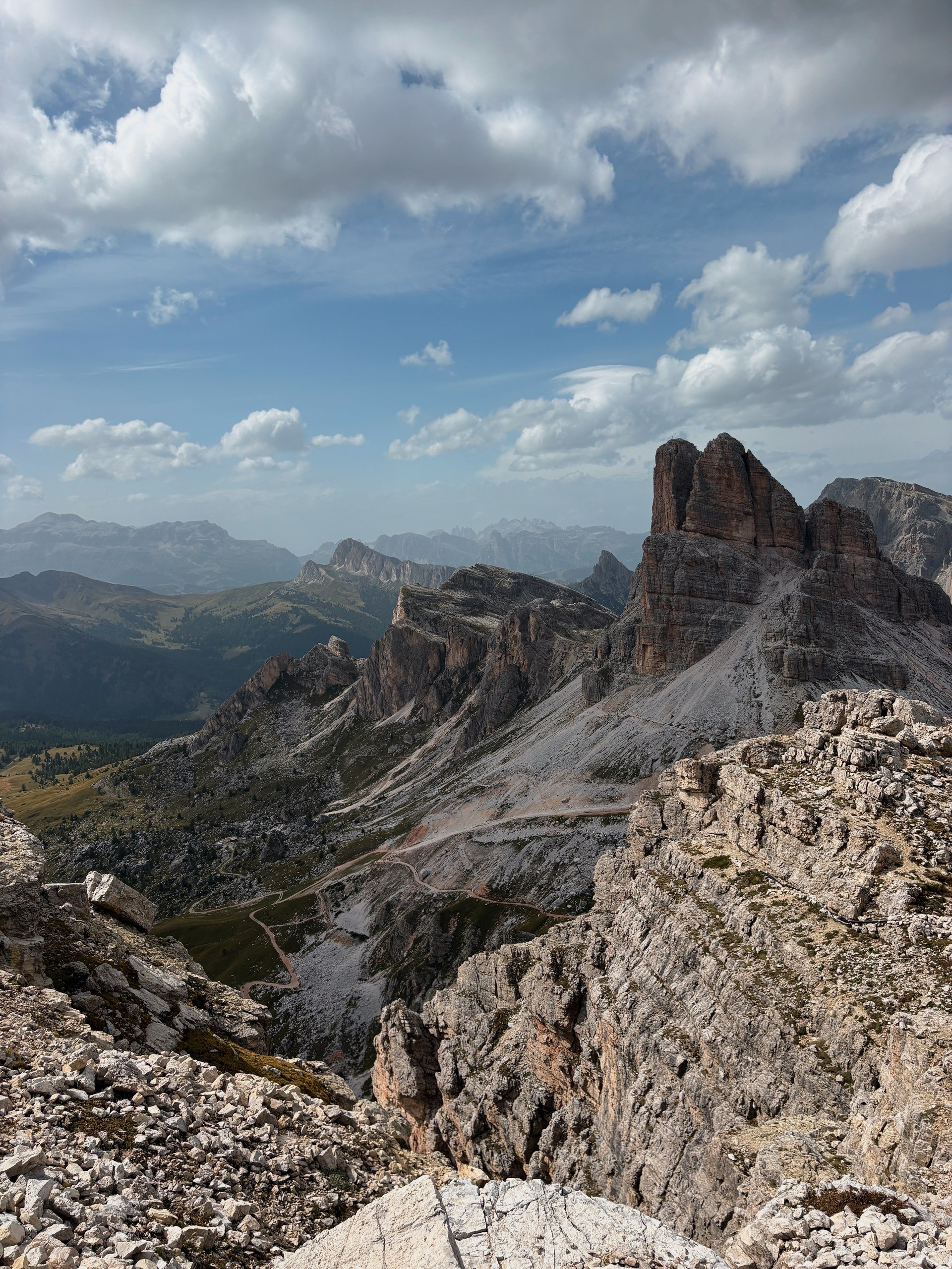 View from a rocky summit toward a towering Dolomites peak under dramatic clouds