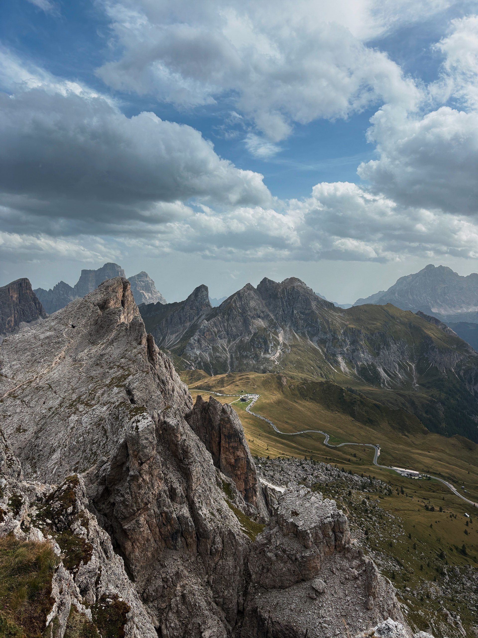 Rocky Dolomites ridge above a winding mountain pass road and green alpine slopes