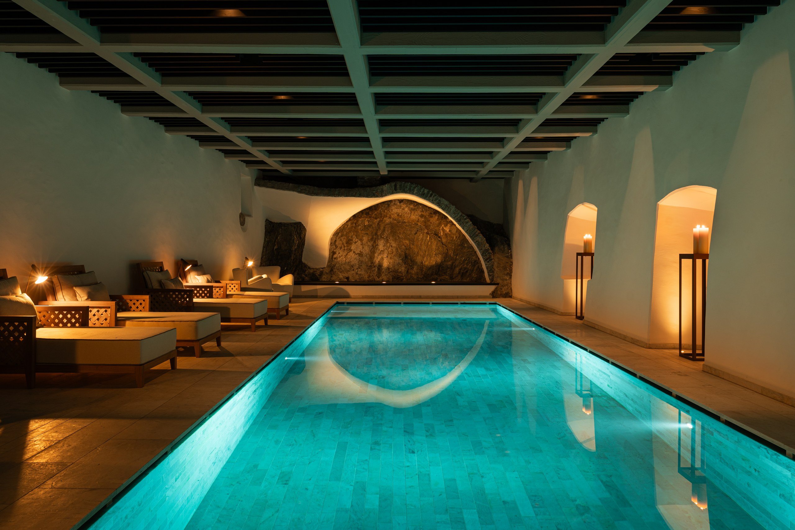 Indoor spa pool with turquoise water, candlelit loungers, and a coffered ceiling at a Dolomites spa hotel