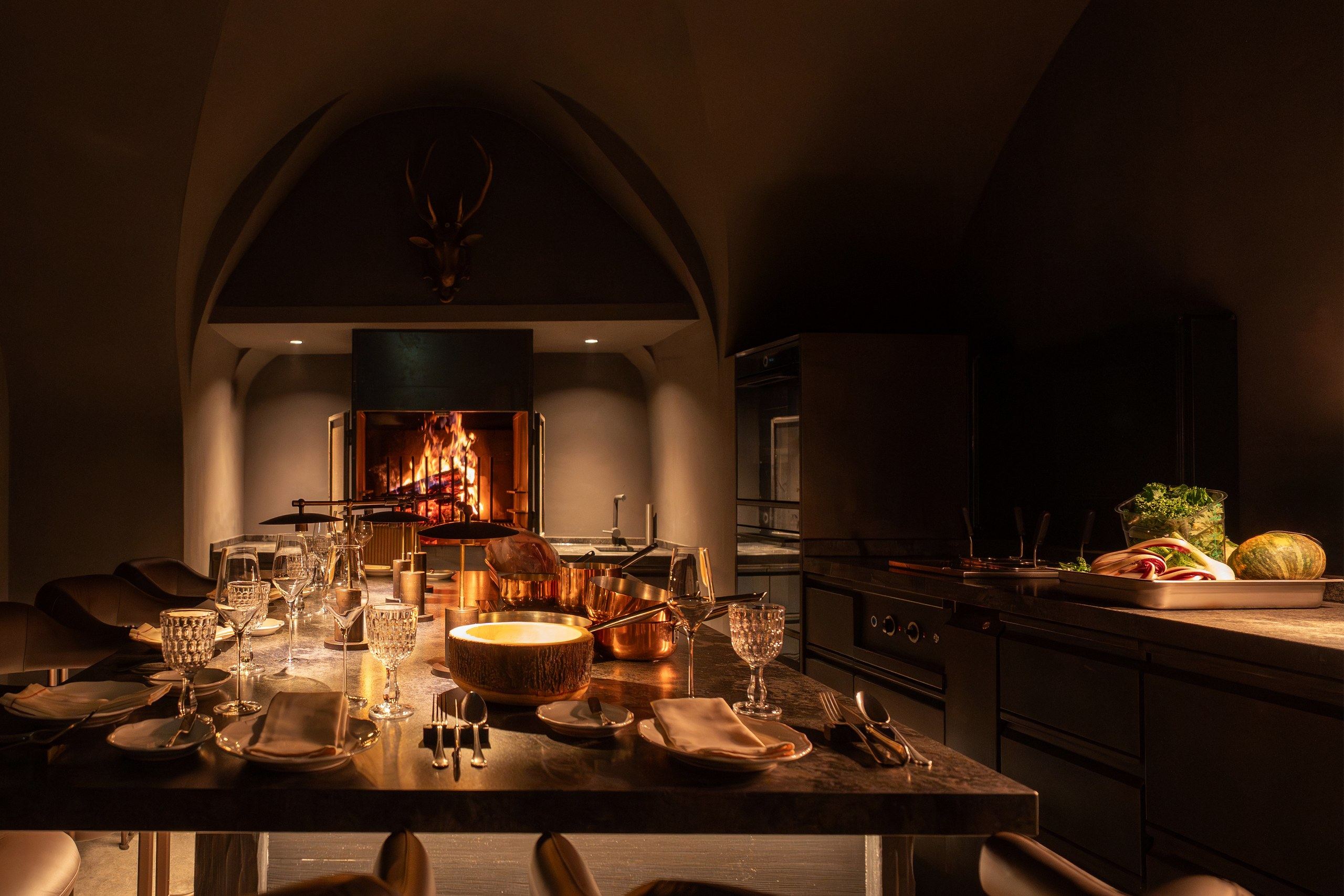 Candlelit chef's table set for a private dinner beside an open fire in a vaulted kitchen in the Dolomites