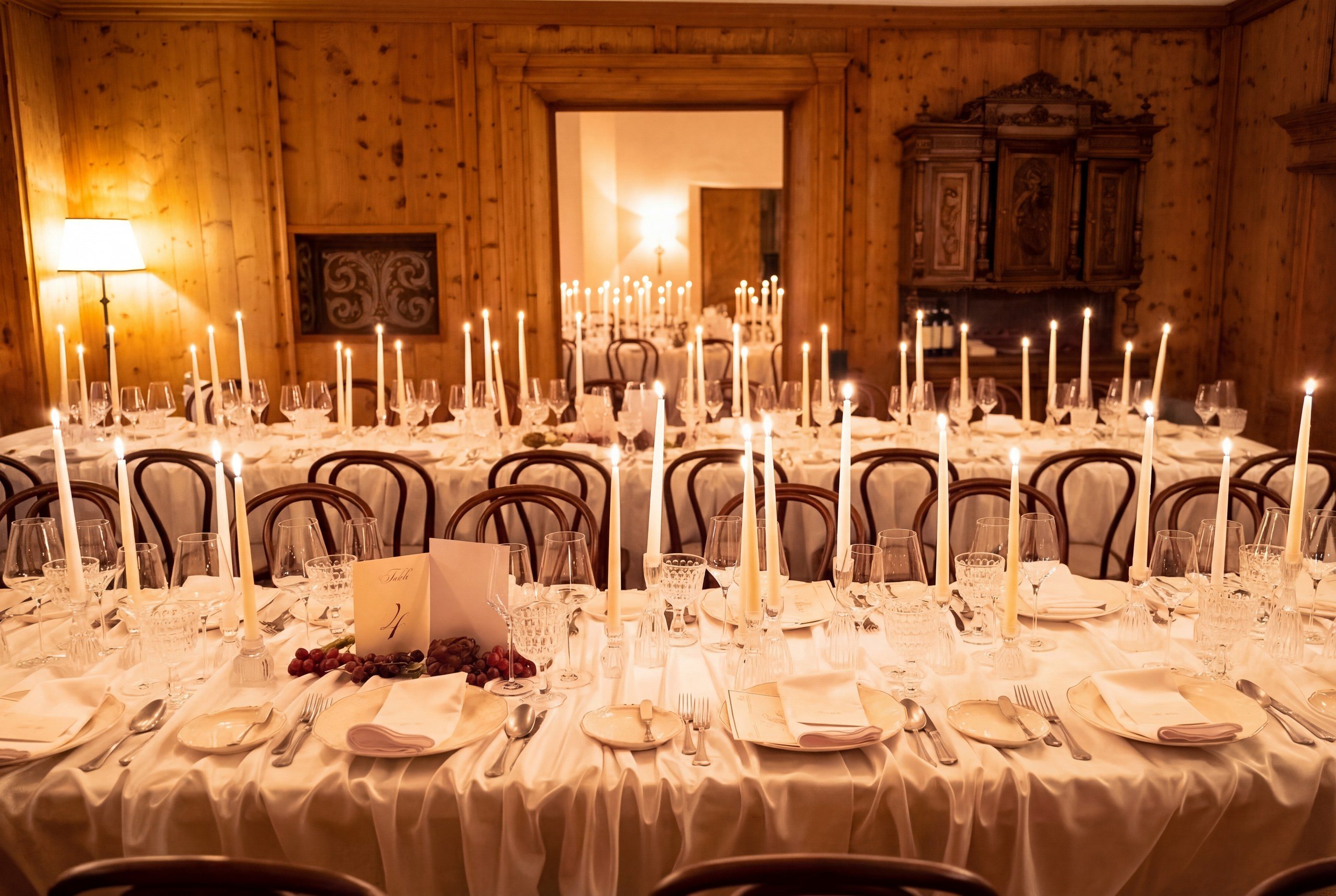 Candlelit wedding reception tablescape with white linens, taper candles, and crystal glassware in a wood-paneled room