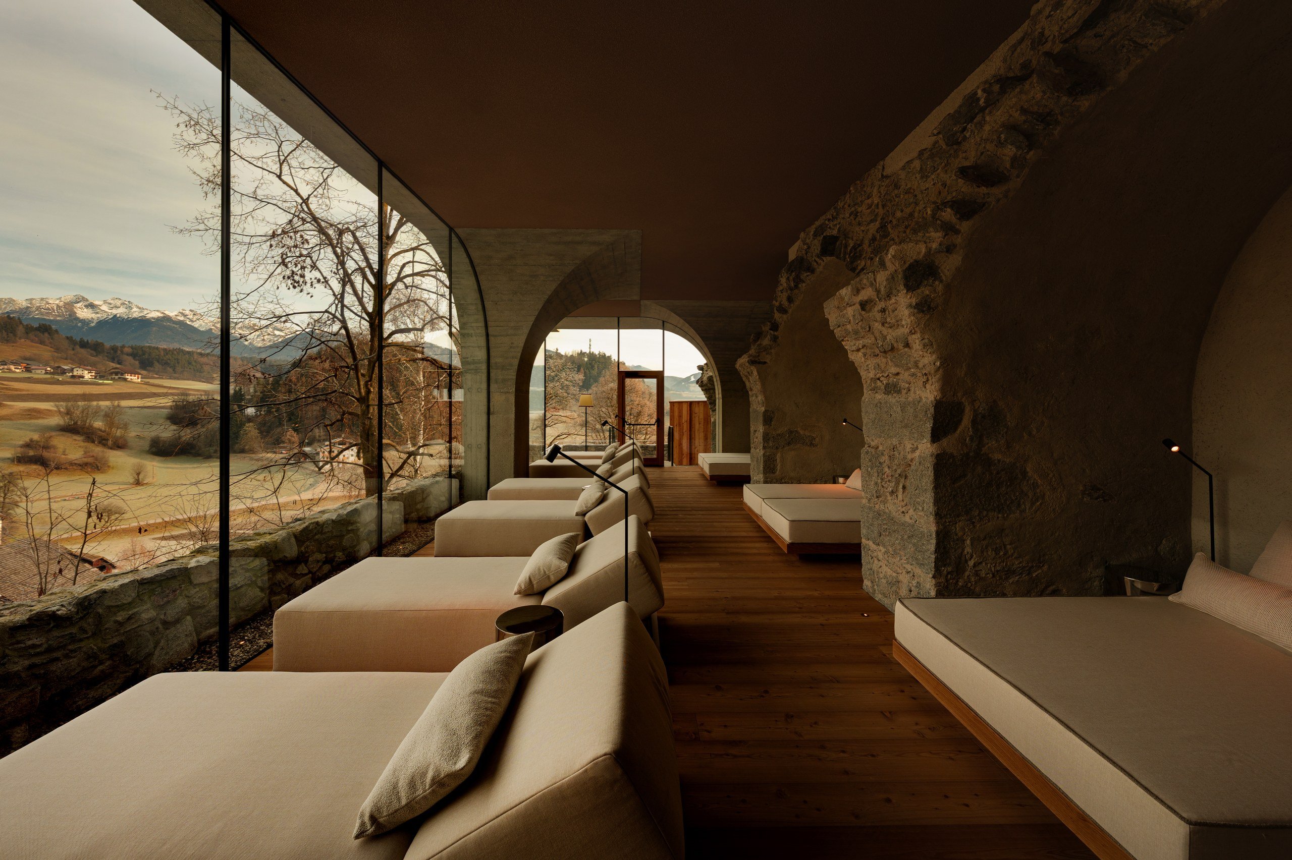Spa relaxation lounge with daybeds along a glass wall facing the valley and snow-capped Dolomites peaks