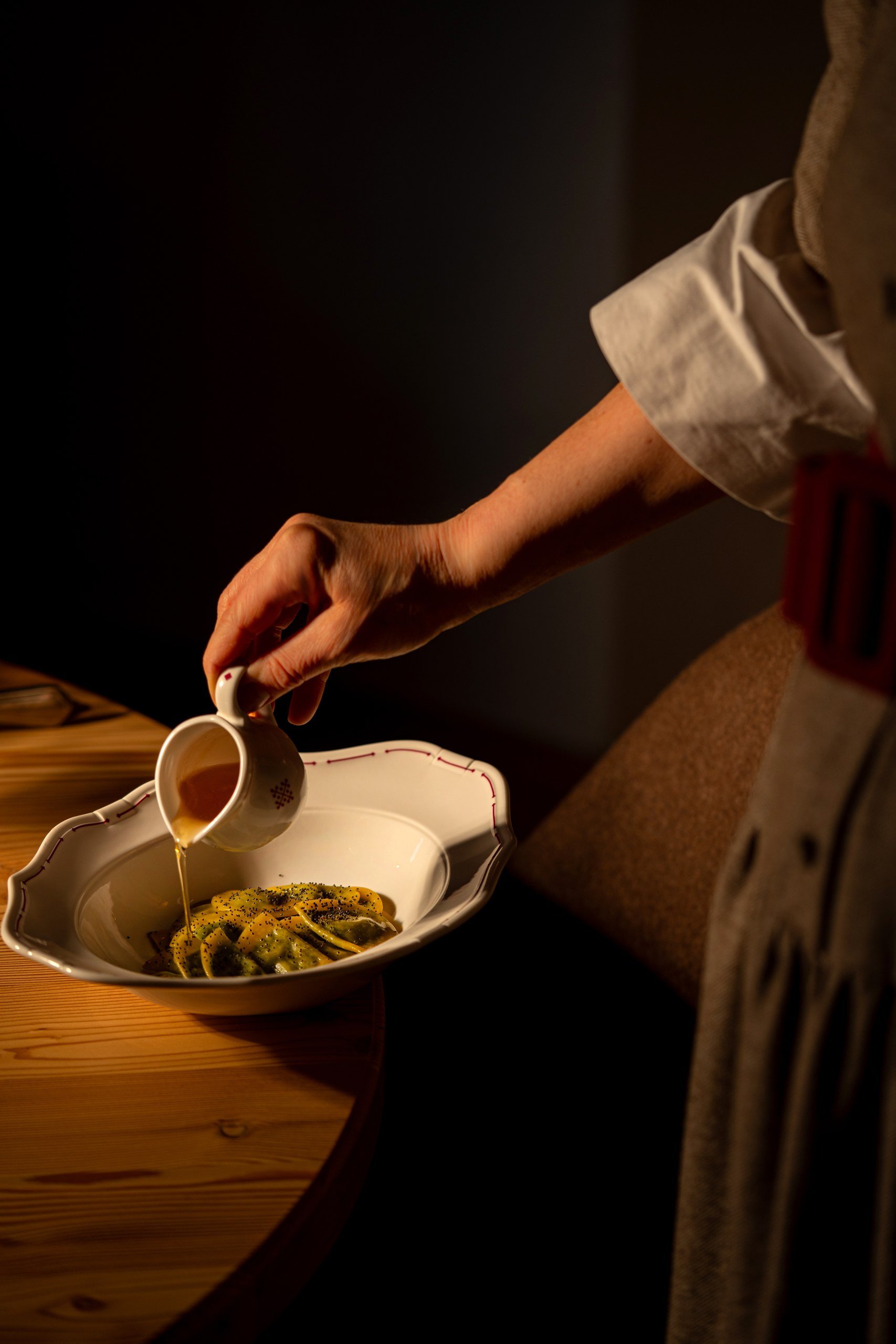 Server pouring sauce over a South Tyrolean pasta dish at a wooden table